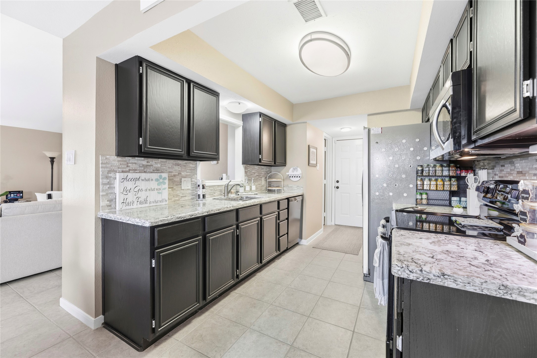 16913 Chapel Pines Drive, Unit 126 Spring, TX 77379 - Photo 11 of 27 This modern kitchen features sleek dark cabinetry, light granite countertops, and a stylish tile backsplash. It includes stainless steel appliances and ample counter space, offering a bright, functional area for cooking and entertaining.