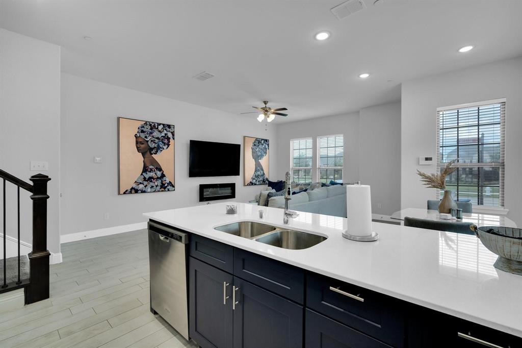 1498 Weston Road Dallas, TX 75234 - Photo 8 of 24 Kitchen island featuring a stainless steel double basin sink, white stone countertop, and dark blue cabinetry with brushed nickel hardware