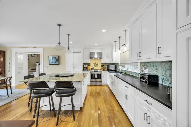 a kitchen with stainless steel appliances kitchen island granite countertop a stove a sink and white cabinets with wooden floor