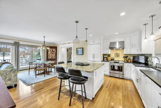 a kitchen with stainless steel appliances kitchen island granite countertop a stove top oven a sink a dining table and chairs with wooden floor