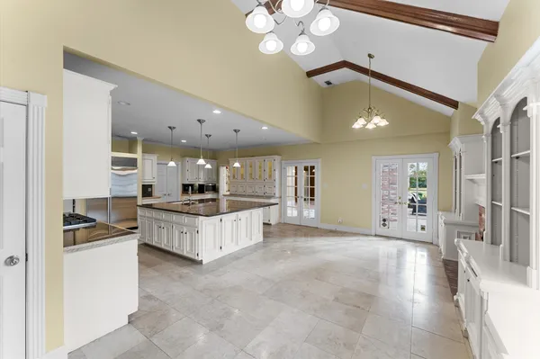 a large white kitchen with kitchen island a large counter space a sink a window and stainless steel appliances