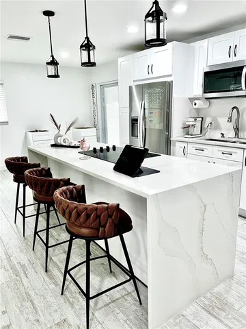 a kitchen with stainless steel appliances kitchen island a table chairs in it and white cabinets