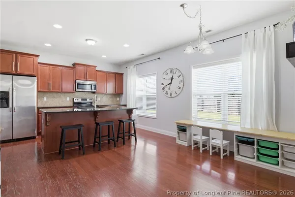 a open kitchen with stainless steel appliances granite countertop a stove top oven a refrigerator a dining table and chairs with wooden floor