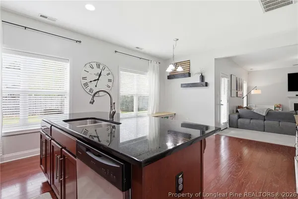 a living room with kitchen island stainless steel appliances a table chairs and a wooden floor