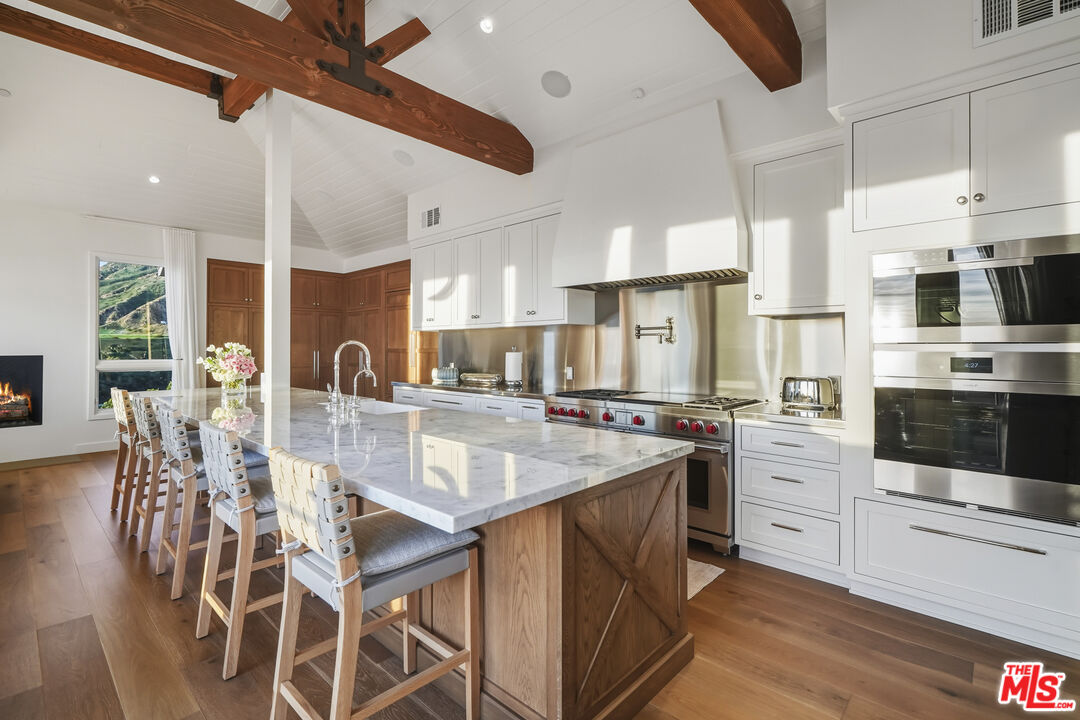 3140 Sweetwater Mesa Road Malibu, CA 90265 - Photo 19 of 71 a kitchen with stainless steel appliances kitchen island granite countertop a table chairs sink and cabinets