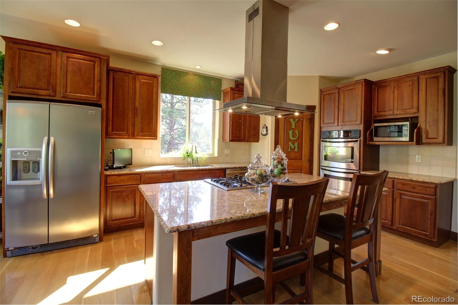 3095 South Piney Ridge Road Evergreen, CO 80439 - Photo 8 of 30 a kitchen with kitchen island granite countertop wooden cabinets and a refrigerator