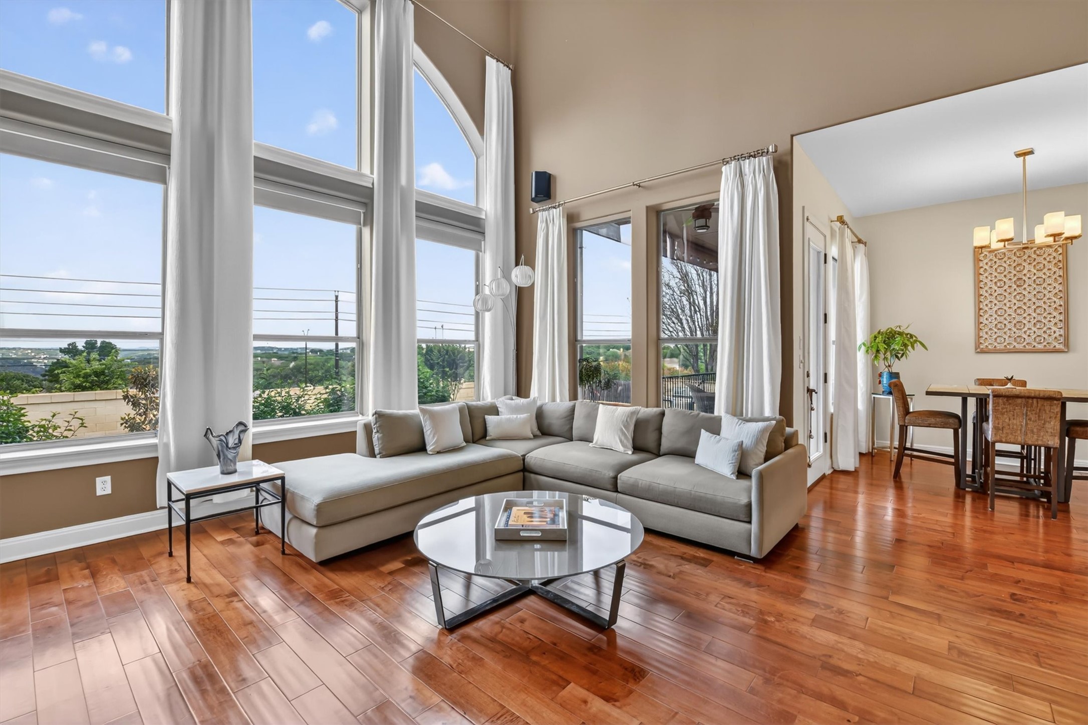 2000 Rio Mesa Drive Austin, TX 78732 - Photo 7 of 39 Living area featuring expansive windows with white curtains, a large sectional sofa, and polished hardwood floors