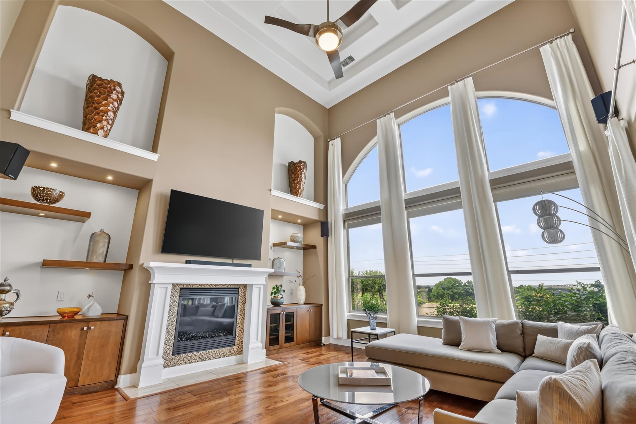 2000 Rio Mesa Drive Austin, TX 78732 - Photo 8 of 39 The living room features high ceilings, hardwood flooring, large arched windows with ample natural light, a fireplace with a decorative tile surround, and a ceiling fan