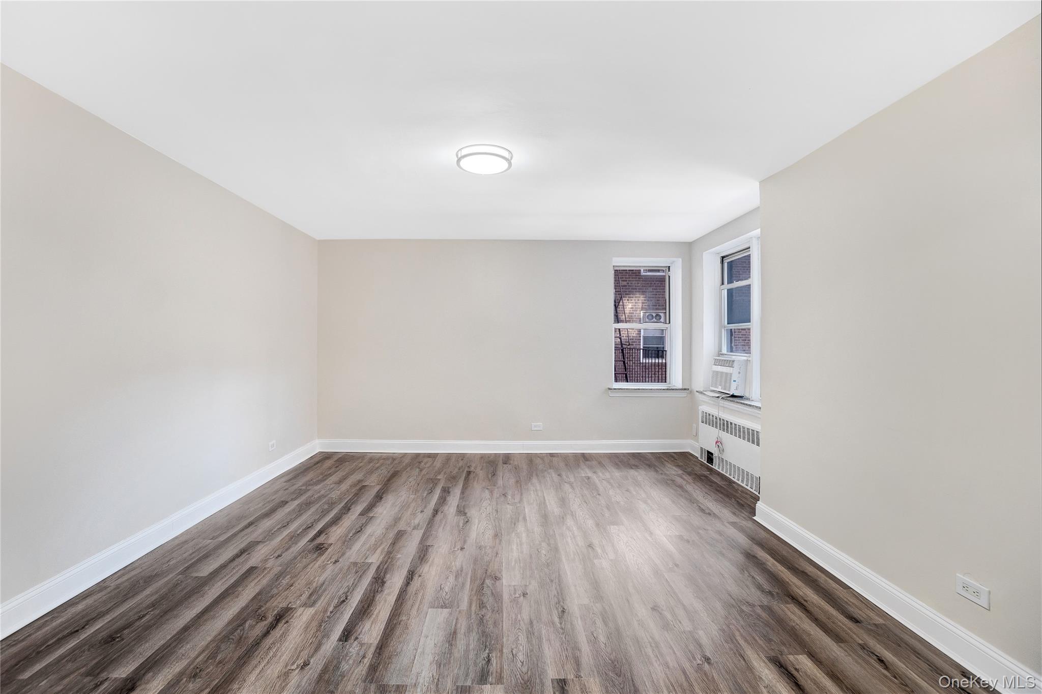 105-24 64th Road, Unit 4L Queens, NY 11375 - Photo 9 of 14 an empty room with wooden floor and windows