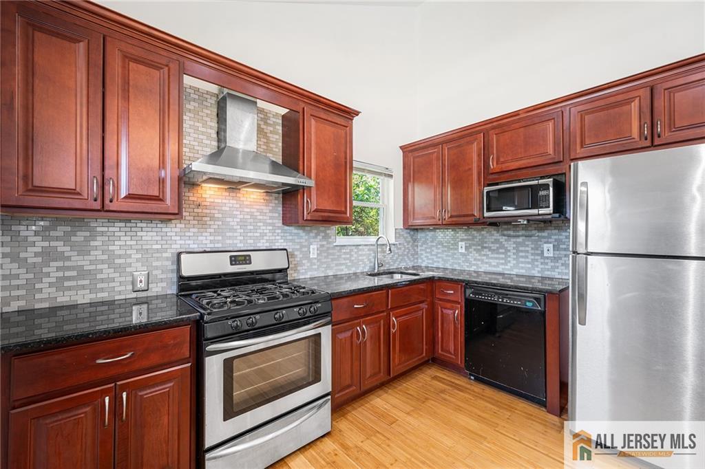 a kitchen with stainless steel appliances granite countertop a stove top oven a sink dishwasher a refrigerator and cabinets with wooden floor