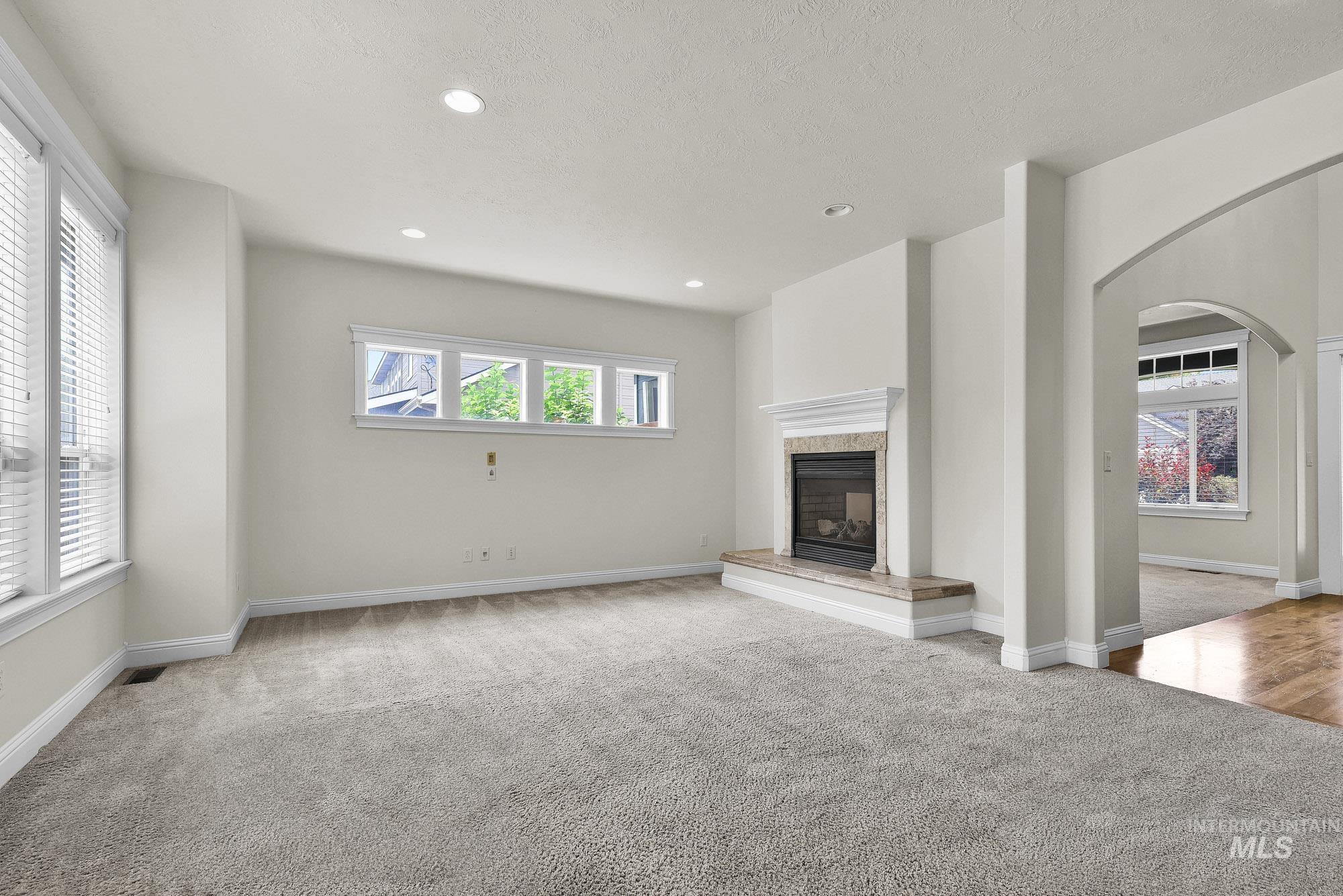 2172 West Cedar Grove Street Meridian, ID 83646 - Photo 7 of 49 Spacious room featuring light-toned carpeting, multiple windows providing ambient illumination, a fireplace with a stone surround and hearth, an ornate mantel, and recessed ceiling lighting