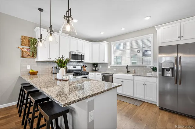 a kitchen with kitchen island granite countertop stainless steel appliances a sink a stove a refrigerator cabinets and dining table