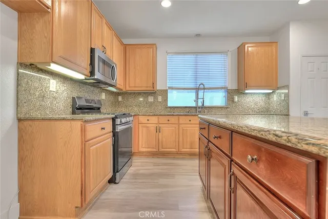 a kitchen with stainless steel appliances granite countertop wooden cabinets a sink and dishwasher a stove with wooden floor