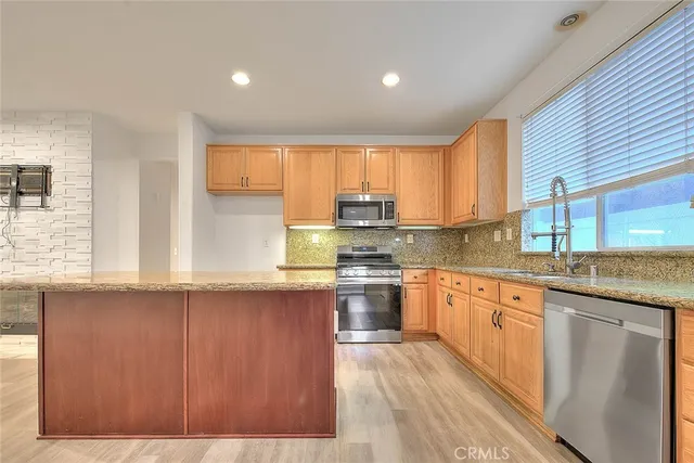 a kitchen with stainless steel appliances granite countertop a stove top oven a sink dishwasher and a refrigerator with wooden floor