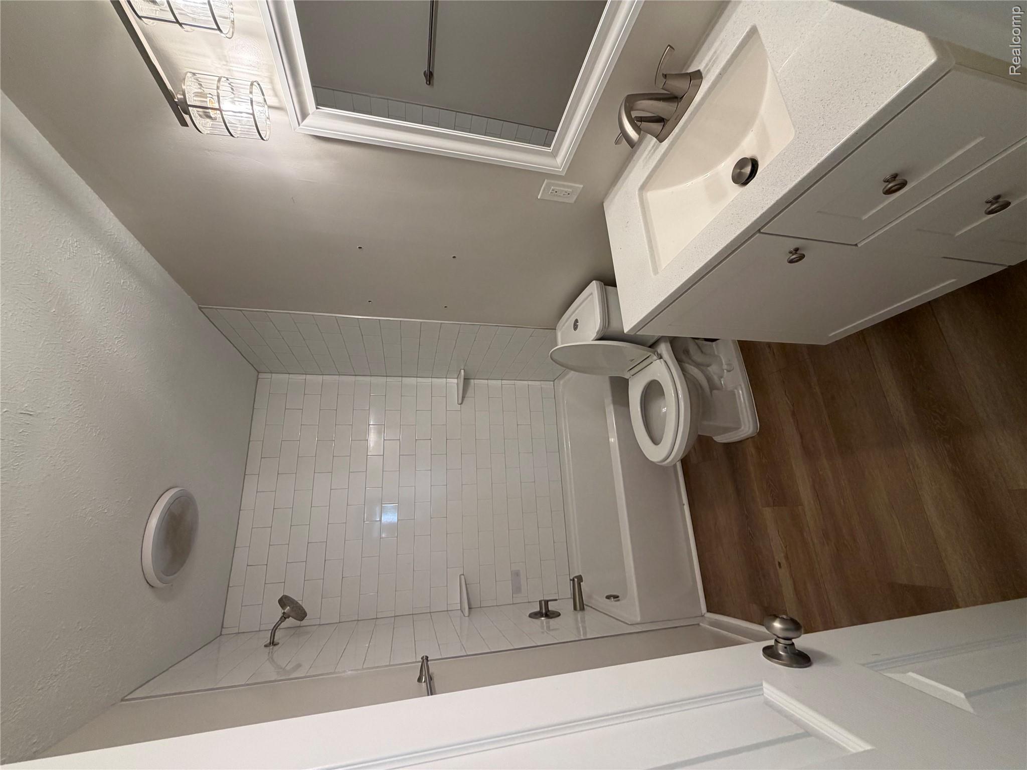 1246 House Road North Webberville, MI 48892 - Photo 6 of 22 White subway tile shower surround with integrated shelves, white vanity with an integrated sink and light-colored countertop, wood-finish flooring, and a framed vanity mirror with an attached light fixture