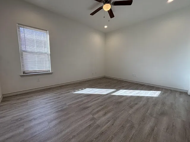 an empty room with wooden floor fan and windows