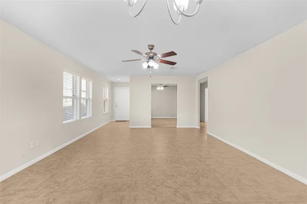 an empty room with chandelier fan and windows