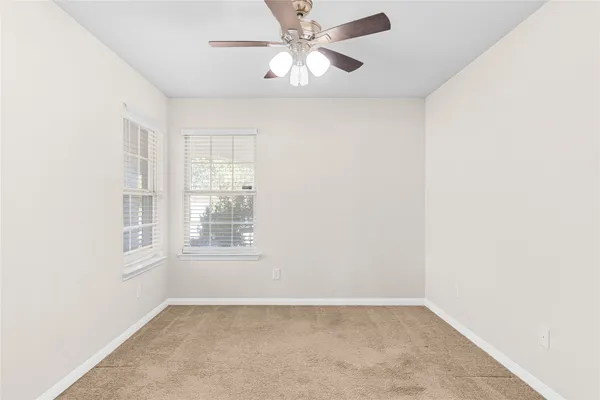 an empty room with chandelier fan and windows