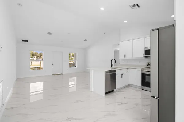 a view of a kitchen with a sink and dishwasher a stove top oven with white cabinets