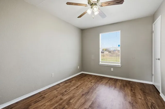an empty room with wooden floor fan and windows
