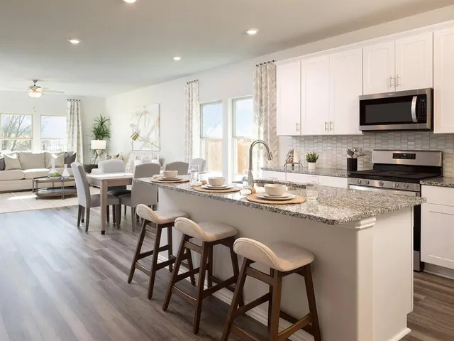 a kitchen with stainless steel appliances granite countertop a stove a sink a microwave a dining table and chairs with wooden floor