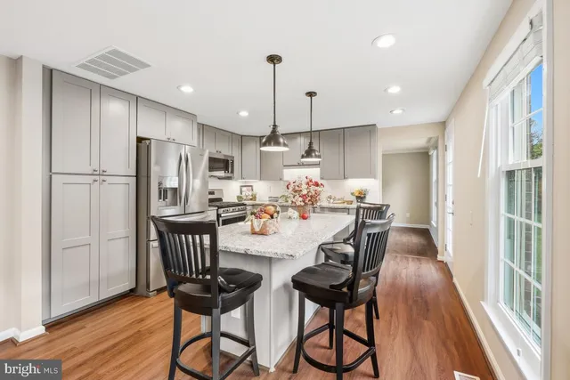 a kitchen with stainless steel appliances a dining table chairs refrigerator and wooden floor