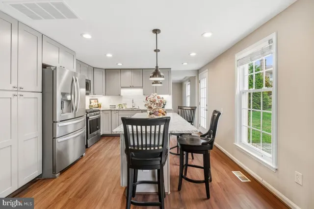 a kitchen with stainless steel appliances a dining table chairs refrigerator microwave and wooden floor