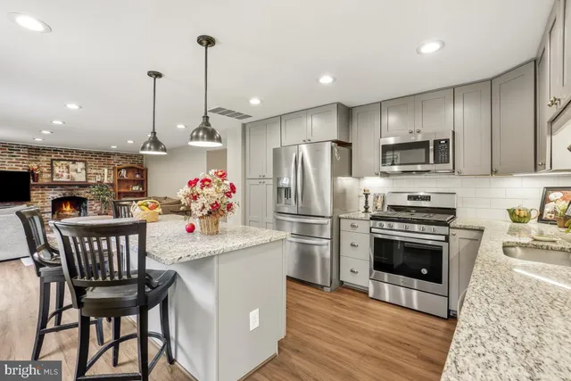 a kitchen with stainless steel appliances kitchen island granite countertop a dining table chairs refrigerator and sink