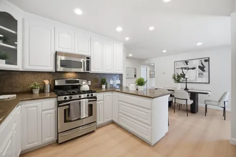 a kitchen with stainless steel appliances granite countertop a stove top oven a sink dishwasher and white cabinets with wooden floor
