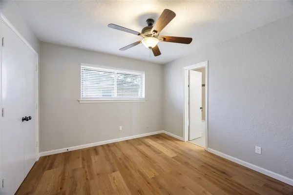 a view of an empty room with wooden floor and a ceiling fan