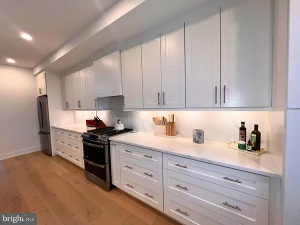 a large white kitchen with a stove a sink a kitchen island with wooden floor and cabinets