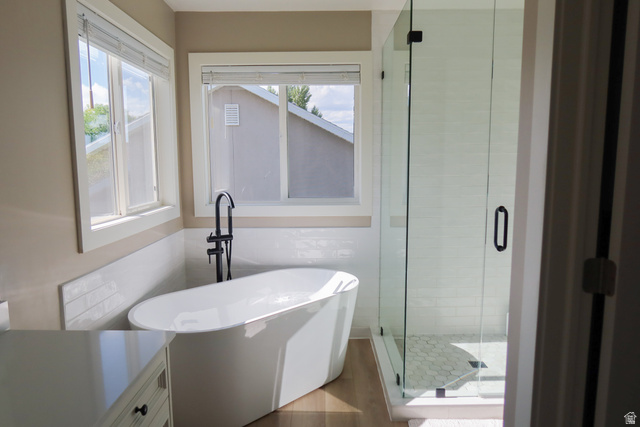 1204 North 3020th Street West Provo, UT 84601 - Photo 27 of 35 Freestanding soaking tub with a floor-mounted matte black faucet, glass-enclosed shower featuring white subway tile, hexagonal tile shower floor, and wood-finish flooring