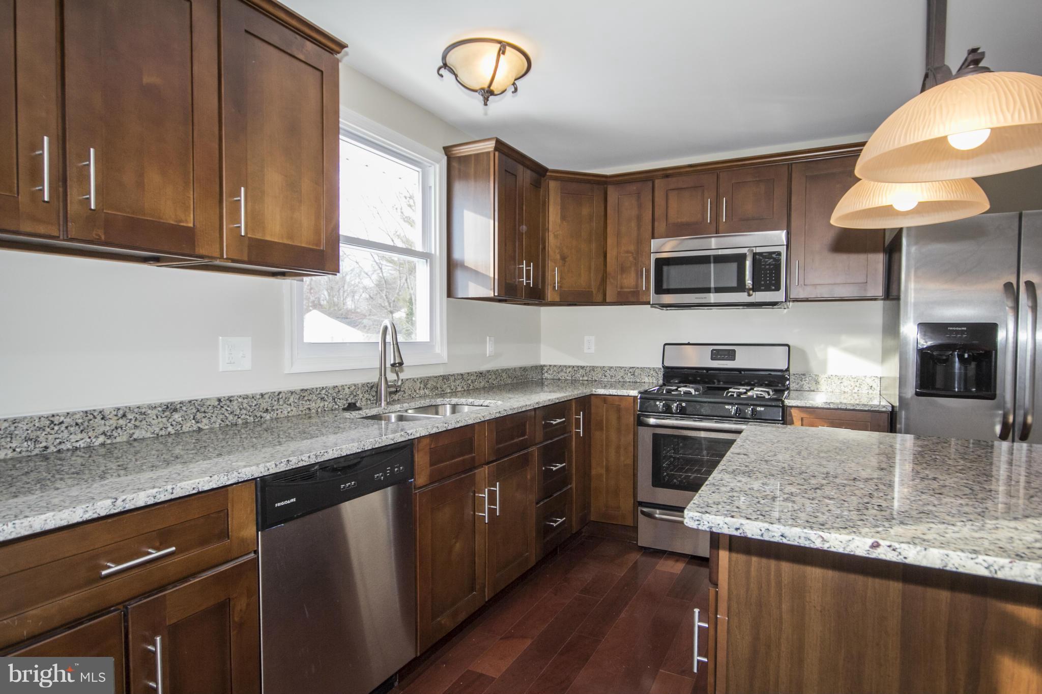 6701 Longhill Road Baltimore, MD 21207 - Photo 3 of 27 a kitchen with stainless steel appliances granite countertop a sink a stove a microwave and wooden cabinets