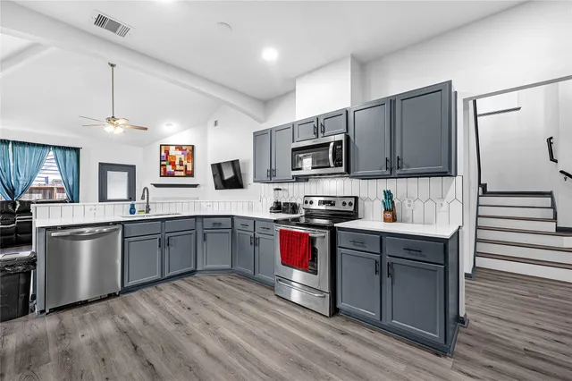 a kitchen with stainless steel appliances granite countertop a refrigerator a stove top oven a sink dishwasher and white cabinets with wooden floor