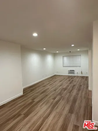 a view of empty room with wooden floor and kitchen