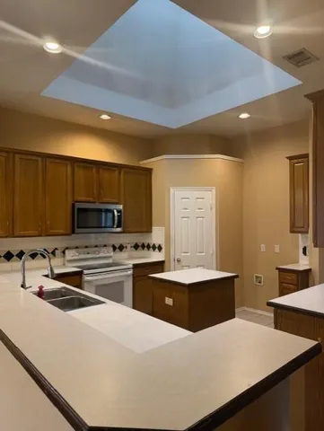 a kitchen with stainless steel appliances a stove a sink a microwave a refrigerator a stove and white cabinets with wooden floor