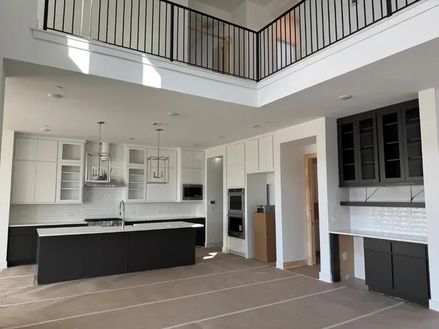 a living room with stainless steel appliances kitchen island granite countertop a refrigerator a sink and a black cabinets