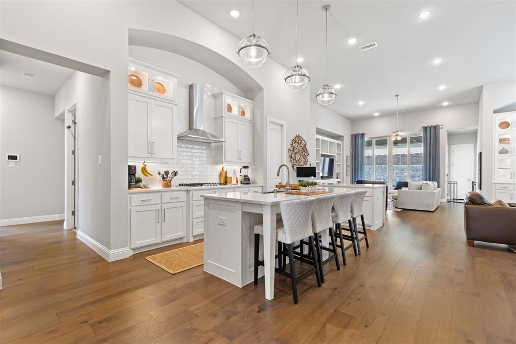 9716 Wilderness Road Little Elm, TX 75068 - Photo 5 of 39 Open-concept living space featuring wood-finish flooring, a white kitchen island with counter seating, pendant lighting, recessed lighting, and white cabinetry