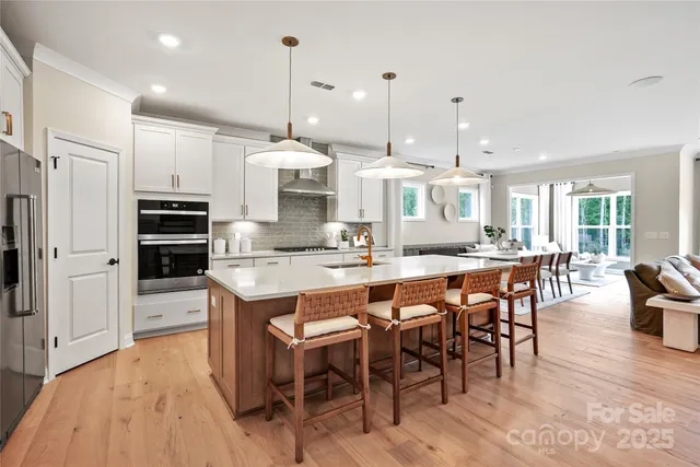 a kitchen with stainless steel appliances granite countertop a stove top oven a refrigerator a dining table and chairs with wooden floor