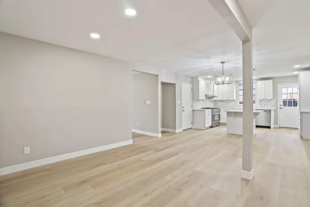 a view of an empty room with wooden floor and a kitchen