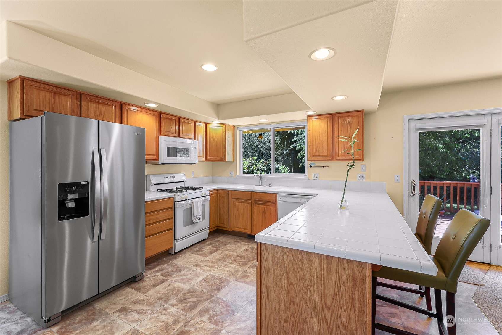 3827 Copper Pond Anacortes, WA 98221 - Photo 6 of 26 a kitchen with stainless steel appliances granite countertop a refrigerator a stove top oven a sink dishwasher a dining table and chairs with wooden floor