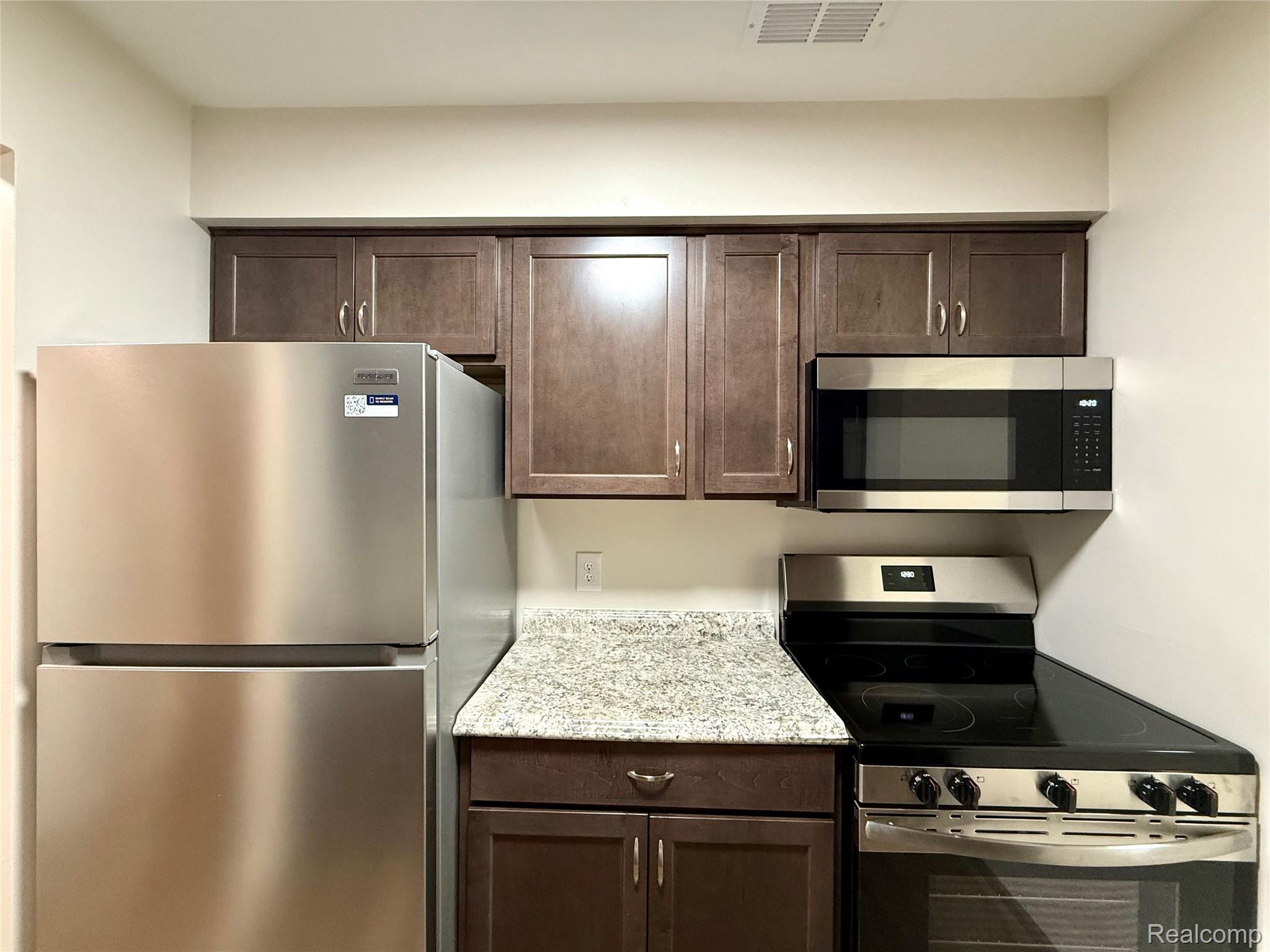 29870 West 12 Mile Road, Unit 703 Farmington, MI 48334 - Photo 8 of 40 Kitchen featuring stainless steel appliances, wood-finish cabinetry, speckled countertop, and overhead ventilation