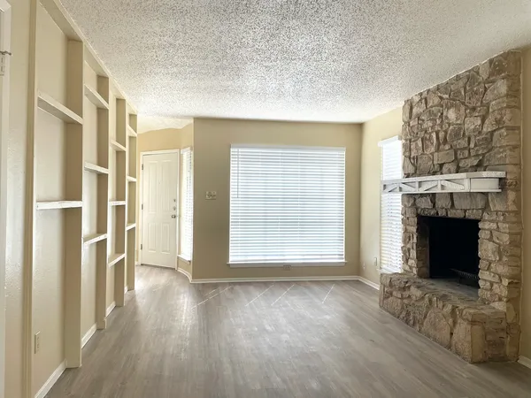 an empty room with wooden floor fireplace and windows