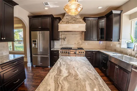 a kitchen with stainless steel appliances granite countertop a refrigerator a sink dishwasher a stove and a dining table with wooden floor