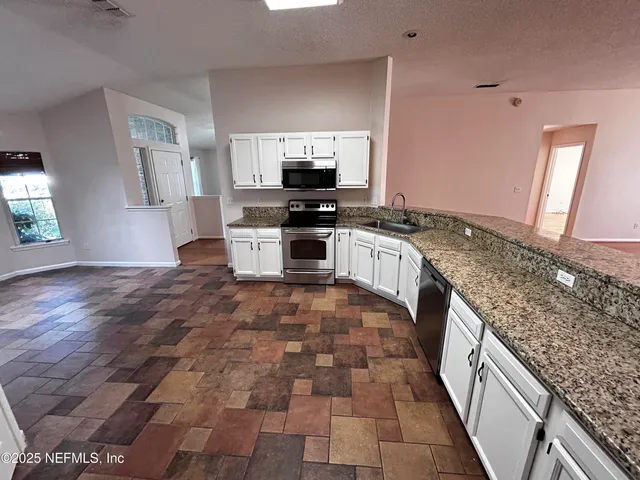 a large kitchen with granite countertop a stove a sink a counter space and cabinets