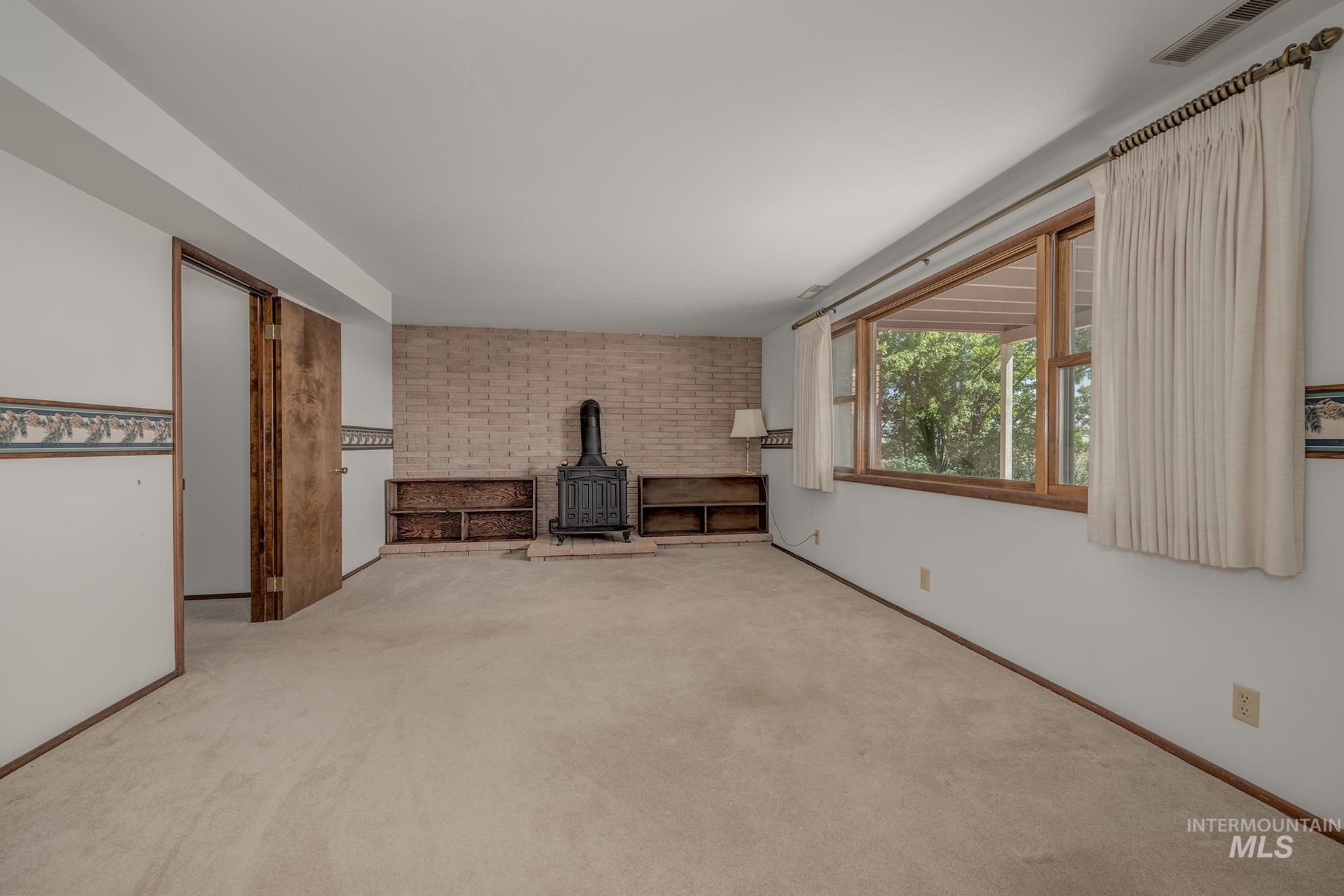1493 Cove Road Weiser, ID 83672 - Photo 31 of 50 Spacious interior featuring neutral carpeting and a prominent brick-clad wall with a dark wood-burning stove
