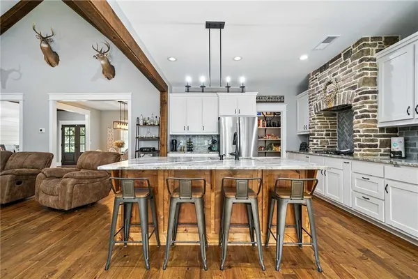 a kitchen with stainless steel appliances kitchen island granite countertop a refrigerator a stove a sink with island chairs and wooden floor