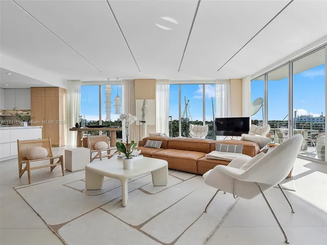 a living room with furniture a kitchen view and a potted plant