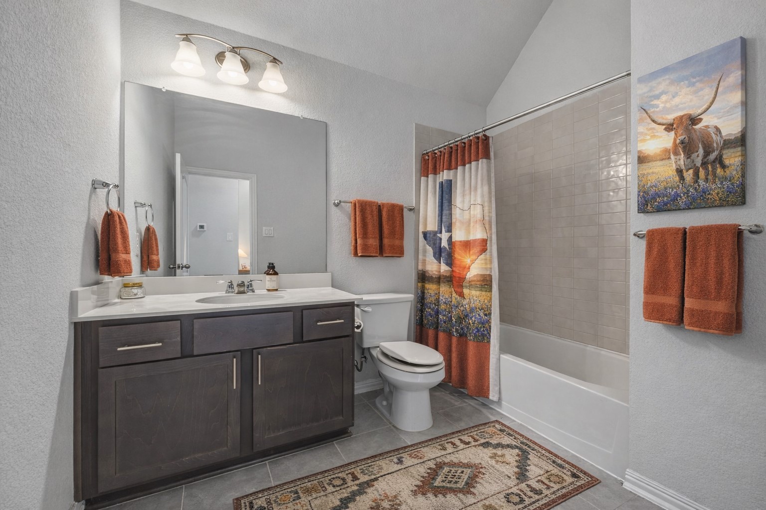 918 Leadtree Loop Buda, TX 78610 - Photo 11 of 27 Bathroom featuring a textured wall, vanity, shower / bath combination with curtain, lofted ceiling, and light tile patterned flooring