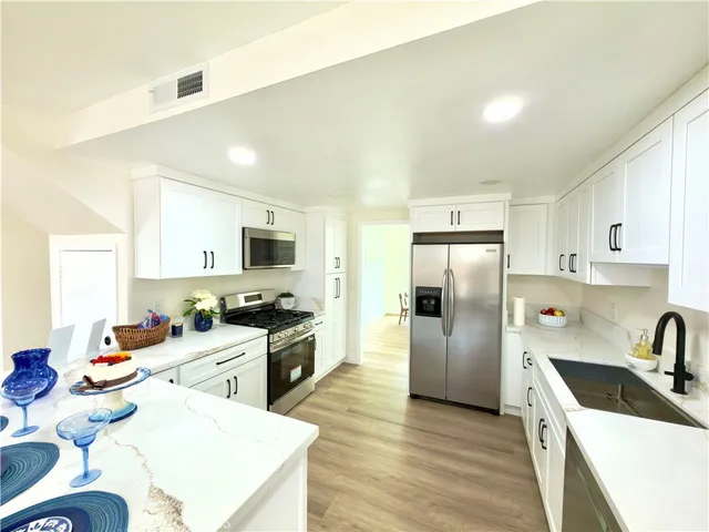 a kitchen with stainless steel appliances kitchen island granite countertop a refrigerator oven a sink dishwasher and white cabinets with wooden floor